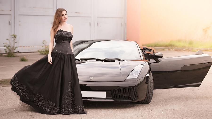 Lady in Black mit Stier - stehende junge Frau im schwarzem Abendkleid vor schwarzem Lamborghini Gallaro mit geöffneter Fahrertüre