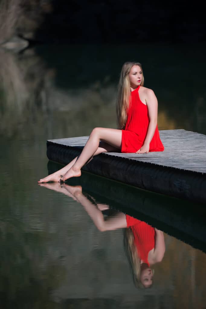 Beauty & Fashion Aufnahme - junge Frau sitzt auf einem Steg am Wasser und spiegelt sich darin