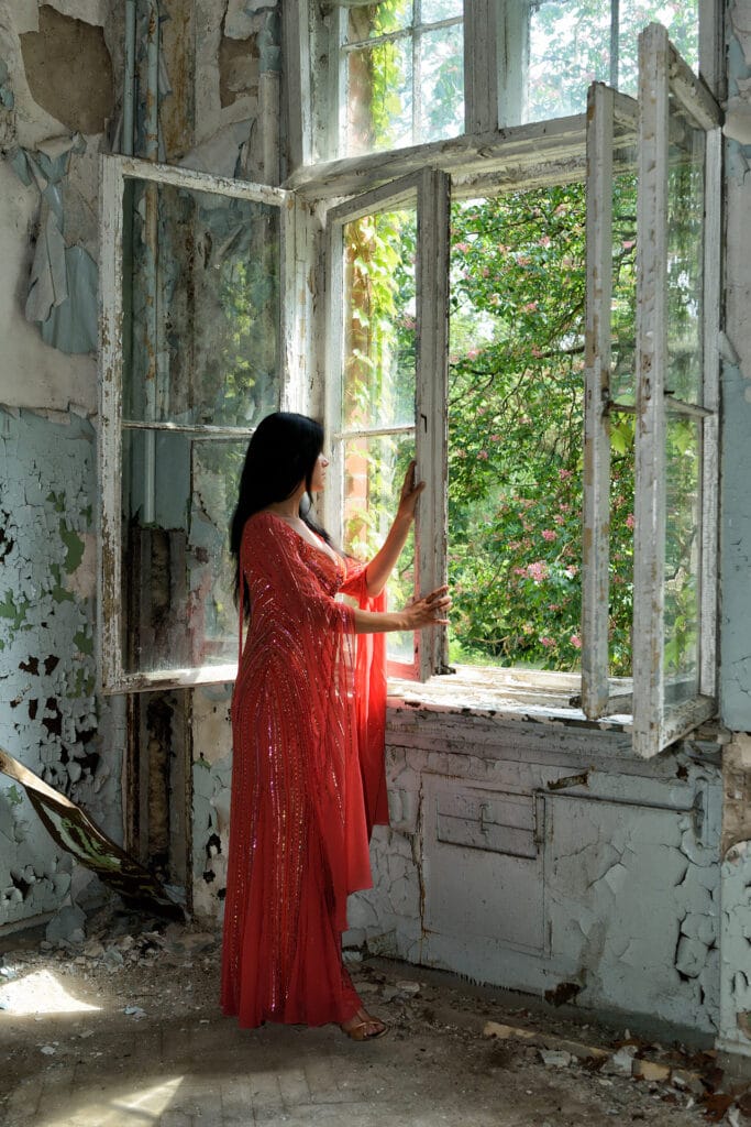 Beauty & Fashion Aufnahme Frau in rotem langen Kleid am Fenster eines verfallenden Hauses