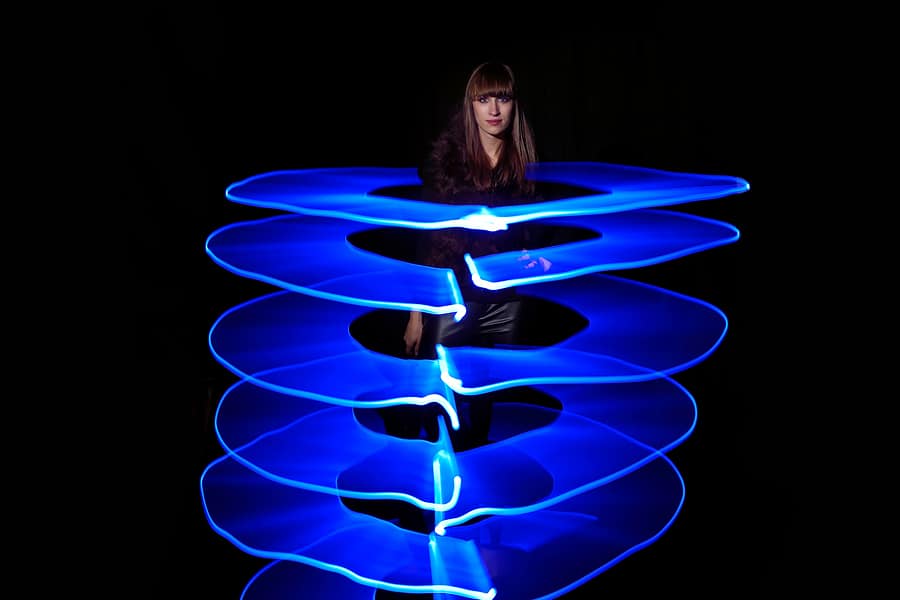 Blue Light Painting - Modell mit ruhigem Ausdruck im Studio vor schwarzem Hintergrund und mit breiter, horizontaler blauer Lichtspur im Kreis um das Modell herum