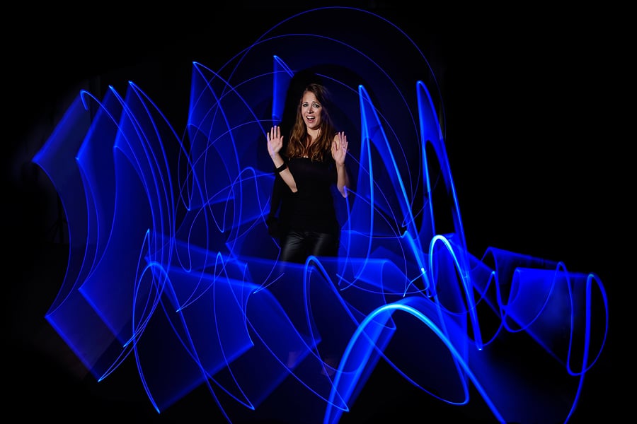 Blue Light Painting - Modell mit ängstlichem Ausdruck und erhobenen Händen im Studio vor schwarzem Hintergrund und mit starker blauer Lichtspur vor und hinter dem Modell