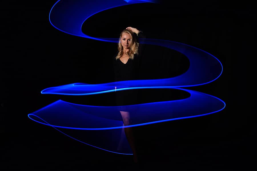 Blue Light Painting - Modell im Studio vor schwarzem Hintergrund und mit blauer gewendelter Lichtspur um das Modell herum