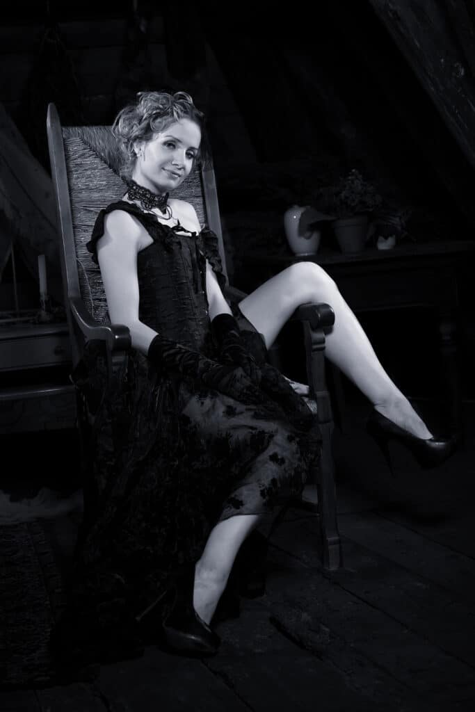 Beauty und Fashionaufnahme - junge Frau in schwarzem Tüllrock und schwarzer Korsage sitzt im Schaukelstuhl und schaut zum Fotografen